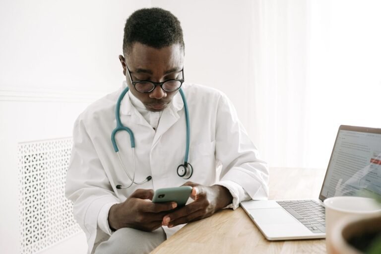 Médico de jaleco usando o celular no consultório